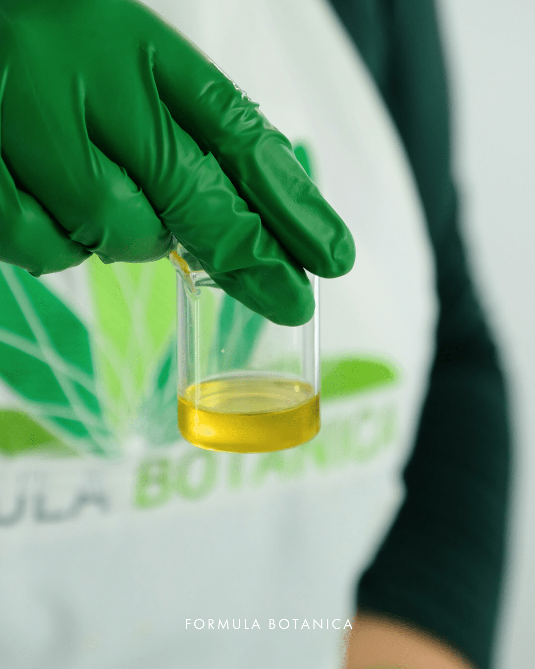 Person holding small beaker of under-eye oil formulation